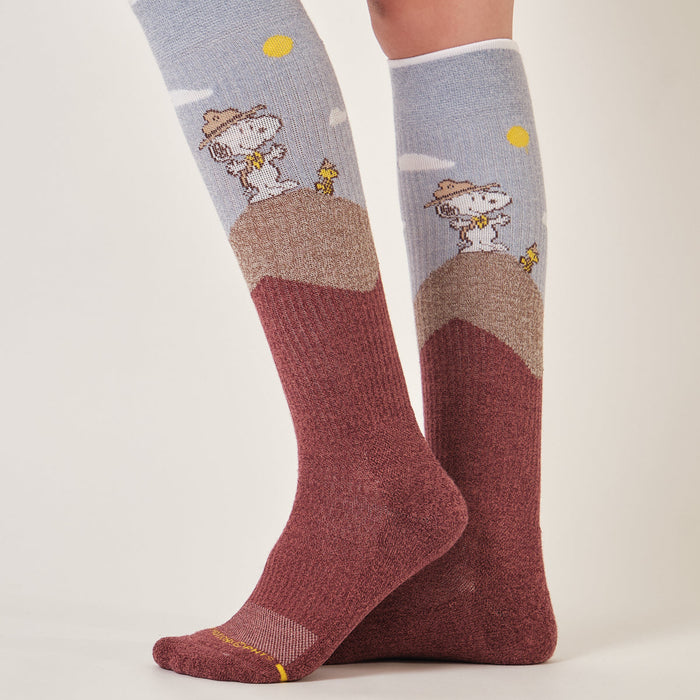 Wine marl knee-high compression socks with a Snoopy mountain hike design, worn in a studio setting.