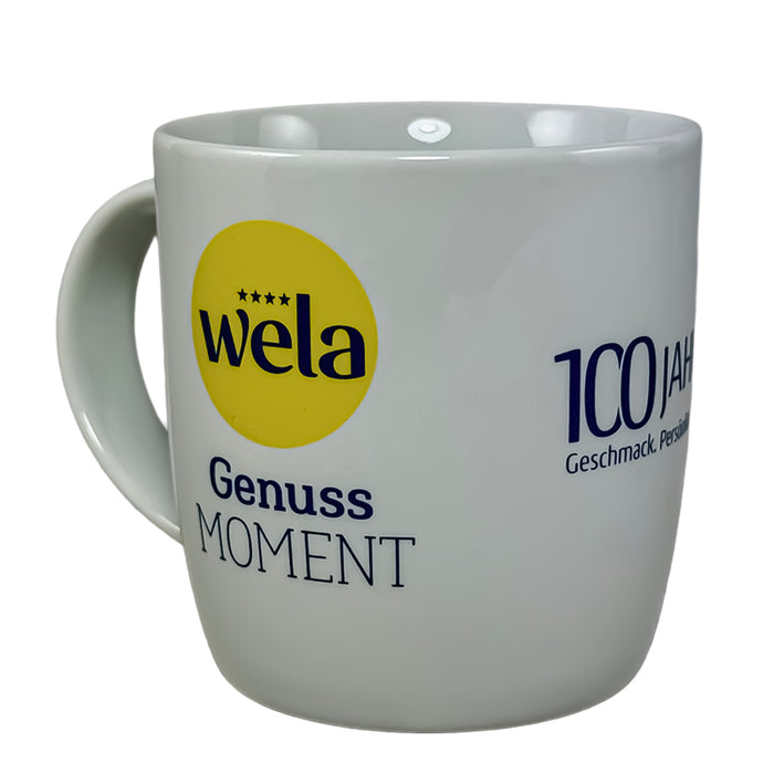 Eine weiße Tasse mit Wela Logo, Schriftzug Genussmoment und 100 Jahre Branding.